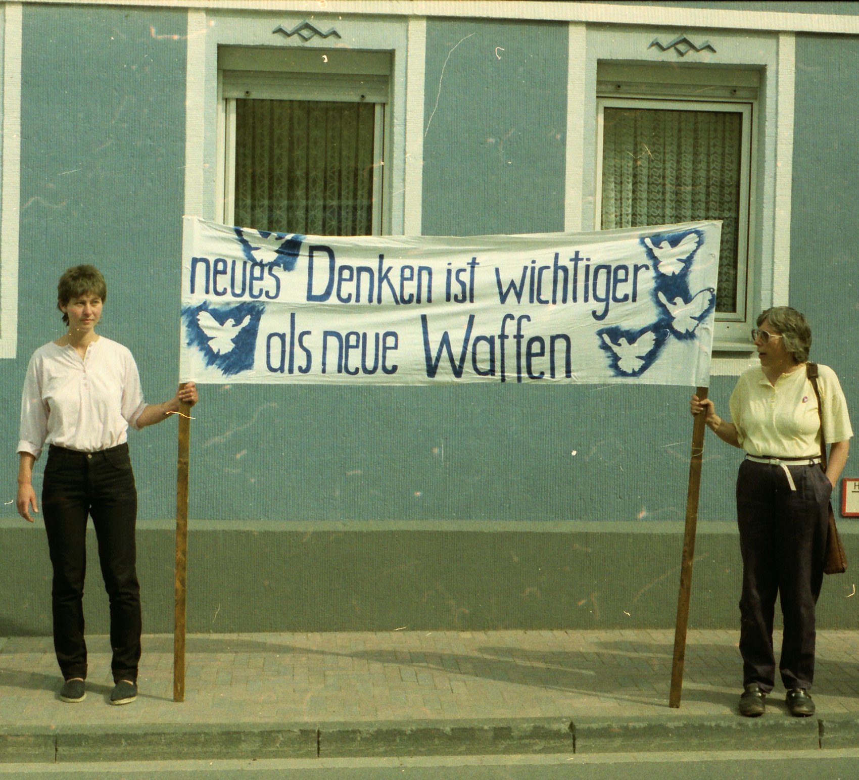 Zwei Frauen halten bei einer Demonstration in Kastellaun 1985 ein Transparent mit der Aufschrift „neues Denken ist wichtiger als neue Waffen“